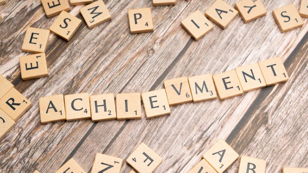 scrabble tiles spelling the word achievement on a wooden surface